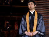 洗える輪袈裟 鬱金の着用イメージ。僧侶が寺院内で輪袈裟を掛けて胸元にかけた正面の記念撮影風カット