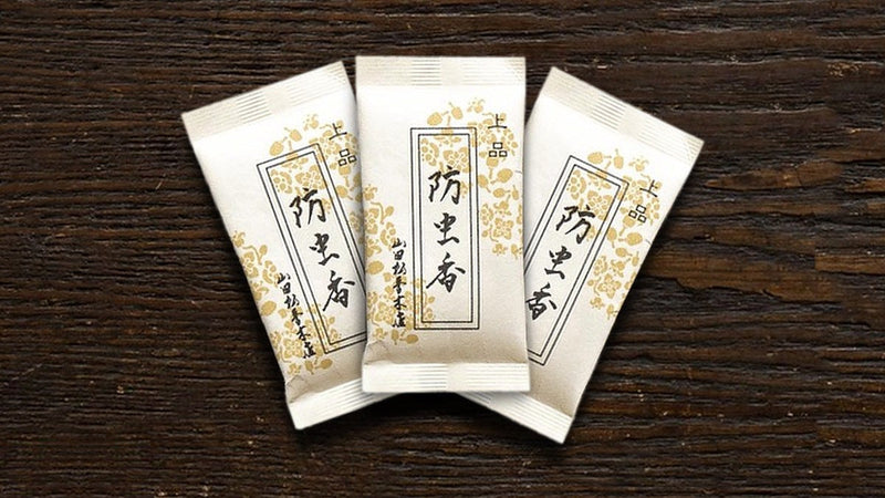 木の台に並べた防虫香の小袋3つ。白地に金の花柄の包みに「上品 防虫香」と書かれている